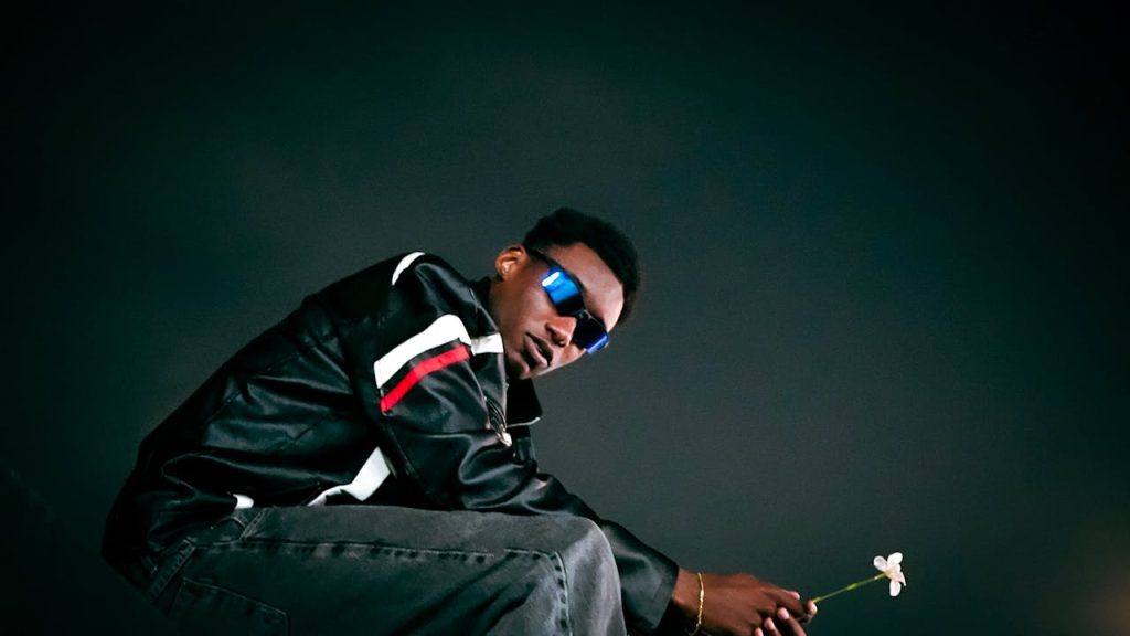 A fashionable individual in a leather jacket poses at night, holding a flower, exuding urban style.