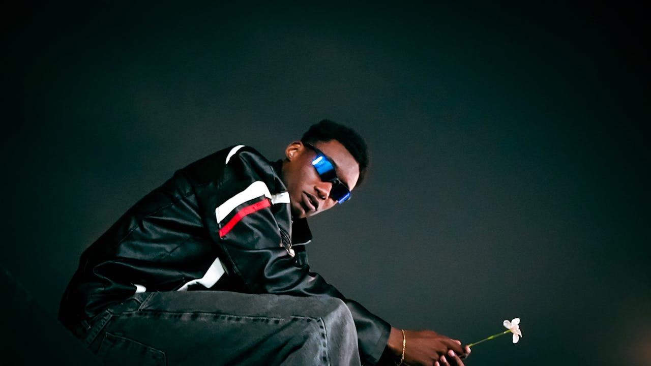 A fashionable individual in a leather jacket poses at night, holding a flower, exuding urban style.